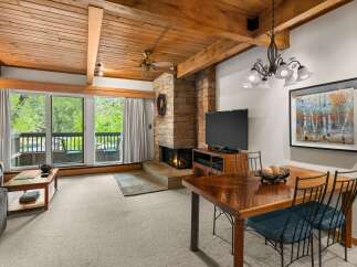 Experience cozy living in this mountain retreat featuring a stunning stone fireplace and a warm, wood-paneled ceiling.