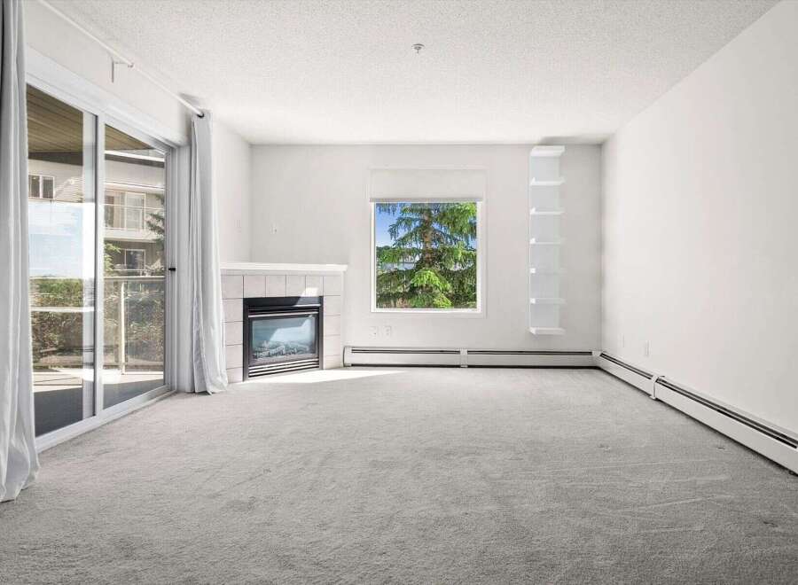 Experience comfortable living in this spacious room featuring a cozy fireplace and a large window offering scenic views of lush greenery.