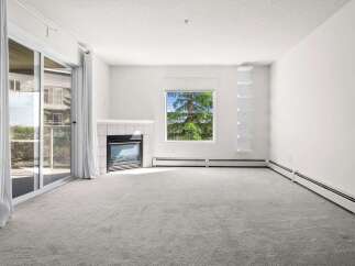 Experience comfortable living in this spacious room featuring a cozy fireplace and a large window offering scenic views of lush greenery.