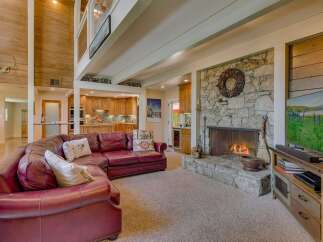Experience rustic charm in this spacious living area, featuring a grand stone fireplace and a soaring wood-paneled ceiling.