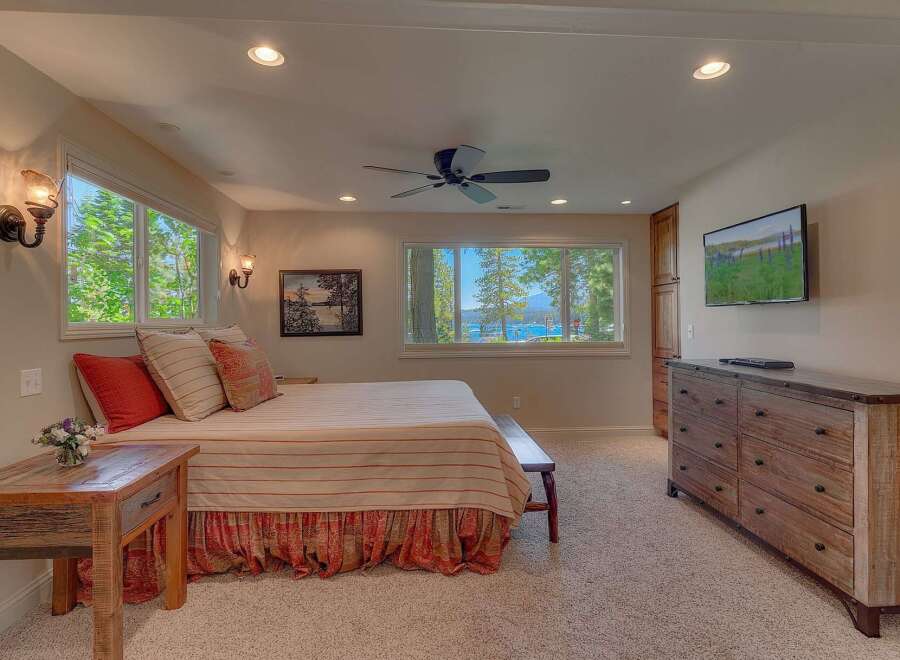 Experience breathtaking lake views from this serene bedroom, featuring a comfortable bed adorned with striped linens and decorative pillows.