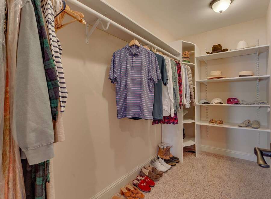 Discover ample storage in this spacious walk-in closet, featuring organized shelving for hats and accessories, along with a well-arranged hanging rod for your apparel.