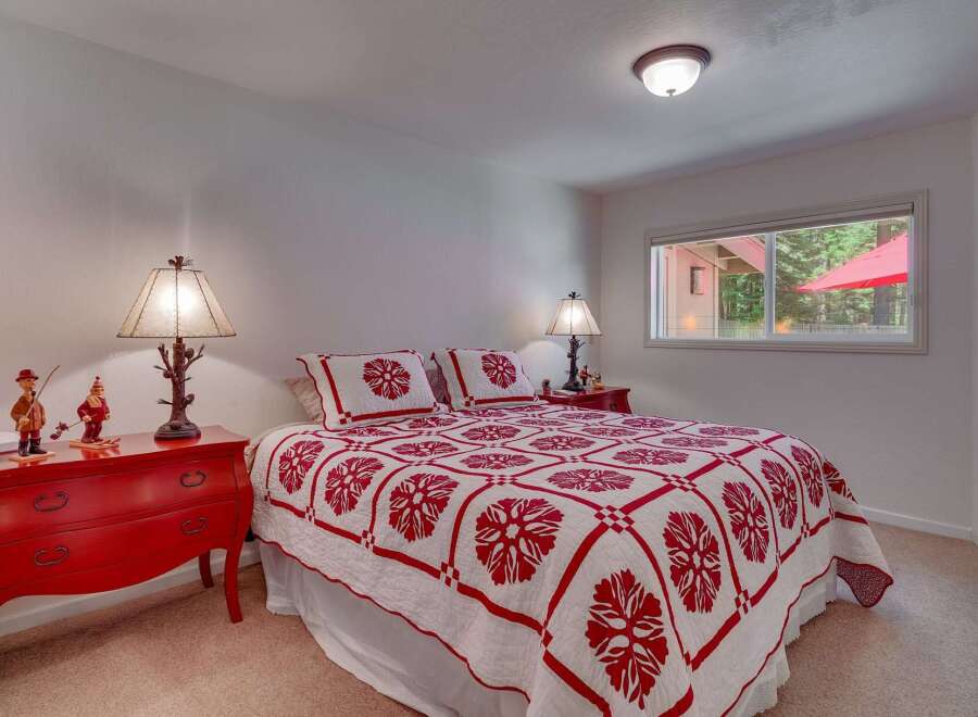 This charming bedroom features a cozy queen-size bed adorned with a striking red and white floral quilt and matching pillows.