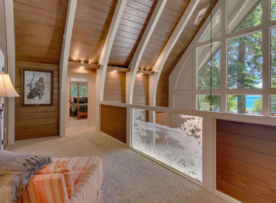 This stunning lakefront property boasts a unique architectural design with a vaulted wood-paneled ceiling and expansive windows offering breathtaking water views.