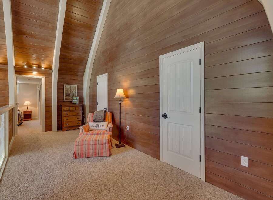 Step into a charming loft area featuring a cozy reading nook with a striped armchair and ottoman, perfect for relaxation.