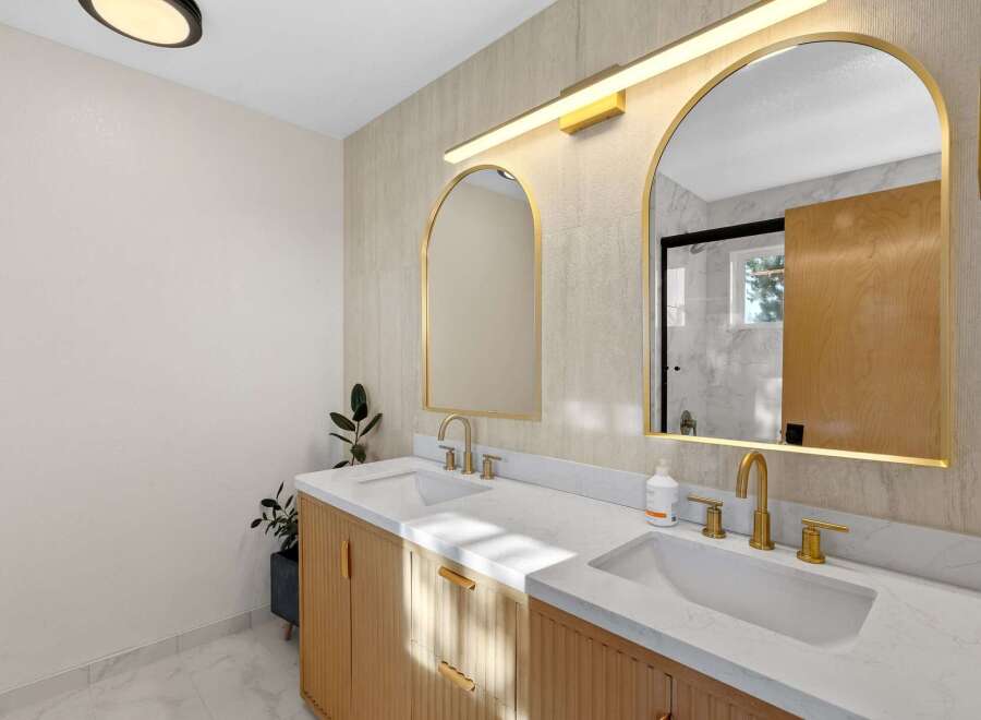 This modern bathroom features a stunning double vanity with fluted wood cabinetry and sleek gold fixtures.