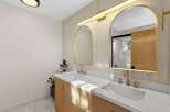 This modern bathroom features a stunning double vanity with fluted wood cabinetry and sleek gold fixtures.