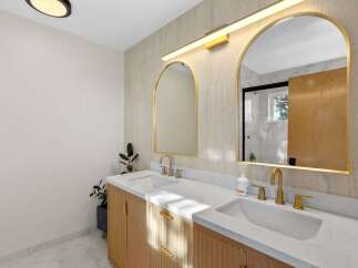 This modern bathroom features a stunning double vanity with fluted wood cabinetry and sleek gold fixtures.