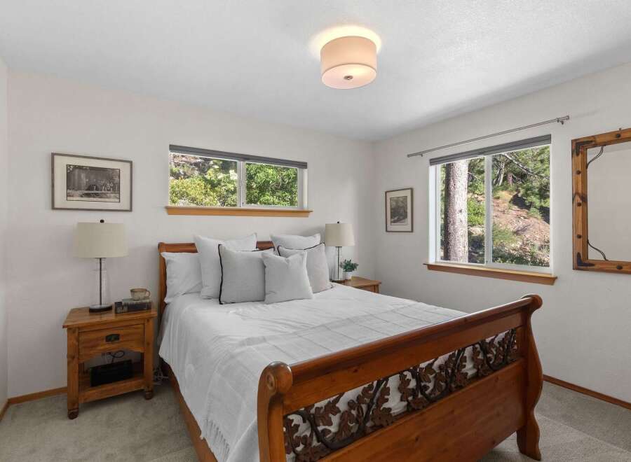 Experience serene living in this charming bedroom, featuring a beautiful wooden sleigh bed and large windows that offer picturesque views of the surrounding natural landscape.