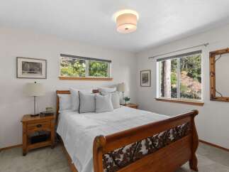 Experience serene living in this charming bedroom, featuring a beautiful wooden sleigh bed and large windows that offer picturesque views of the surrounding natural landscape.