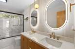 Experience modern luxury in this stunning bathroom featuring a dual vanity with sleek gold fixtures and fluted wood cabinetry.
