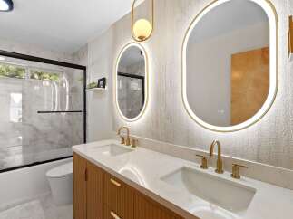 Experience modern luxury in this stunning bathroom featuring a dual vanity with sleek gold fixtures and fluted wood cabinetry.