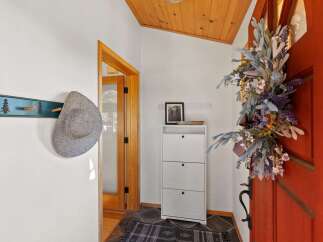 Welcome guests into this charming entryway featuring a rustic coat rack with a stylish hat, a convenient white shoe cabinet, and a beautiful floral wreath adorning the vibrant red door.