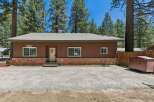 Charming single-story home nestled among tall pine trees, featuring a warm brown exterior with a classic brick foundation.