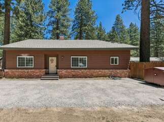 Charming single-story home nestled among tall pine trees, featuring a warm brown exterior with a classic brick foundation.