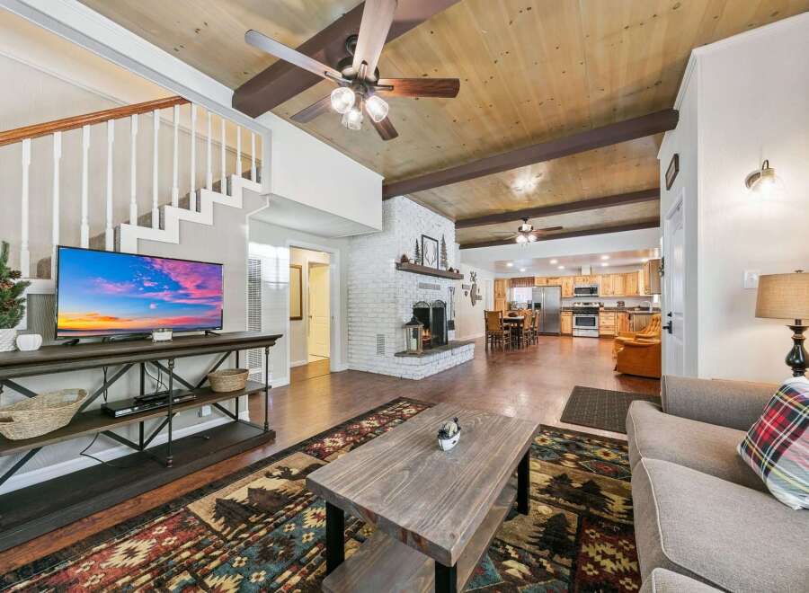 Experience rustic charm in this spacious living area, featuring a cozy brick fireplace and a stunning wood-paneled ceiling with exposed beams.