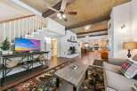 Experience rustic charm in this spacious living area, featuring a cozy brick fireplace and a stunning wood-paneled ceiling with exposed beams.