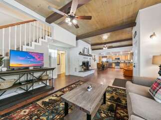 Experience rustic charm in this spacious living area, featuring a cozy brick fireplace and a stunning wood-paneled ceiling with exposed beams.