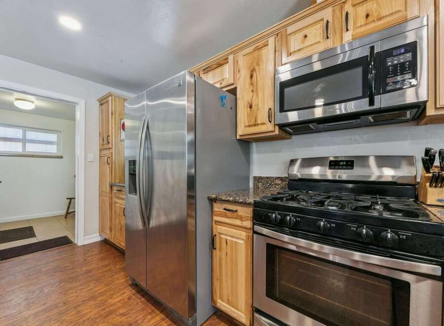 This kitchen features a spacious stainless steel refrigerator, a gas range with a microwave above, and ample natural wood cabinetry.