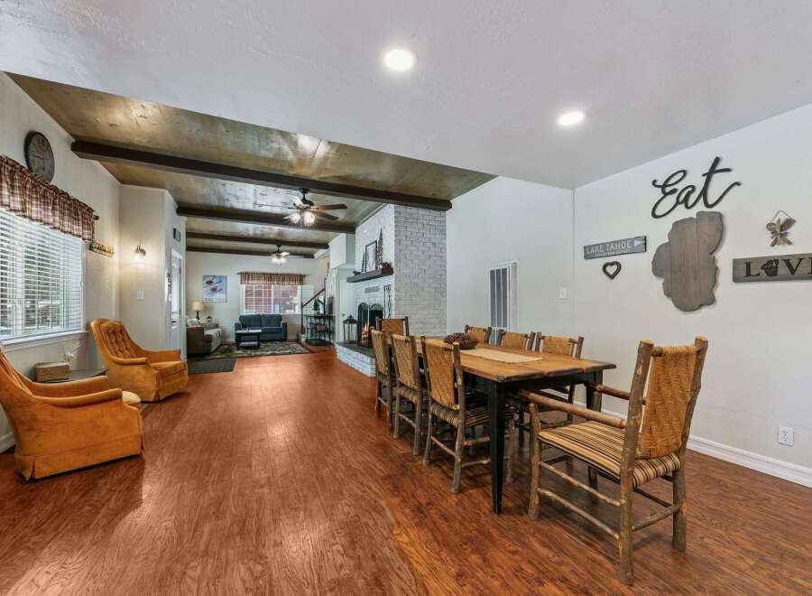 Experience rustic charm in this spacious living and dining area, featuring exposed wooden beams and a cozy brick fireplace.