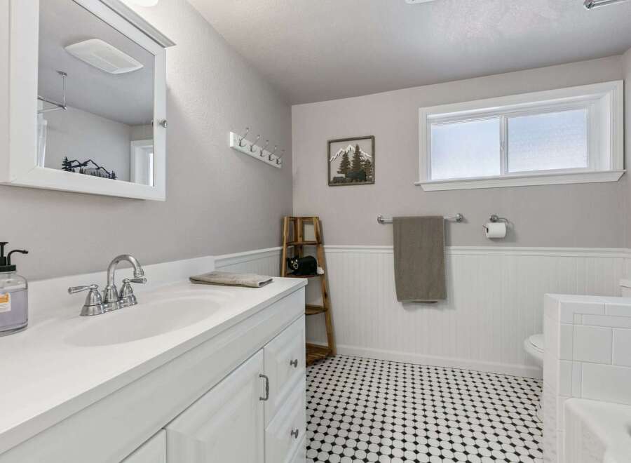 This charming bathroom features a sleek white vanity with a modern chrome faucet, complemented by a large mirror and ample storage.