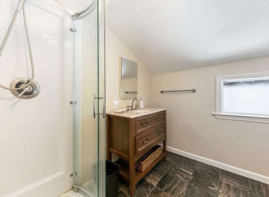 This bathroom features a sleek glass-enclosed shower and a charming wooden vanity with a marble countertop.