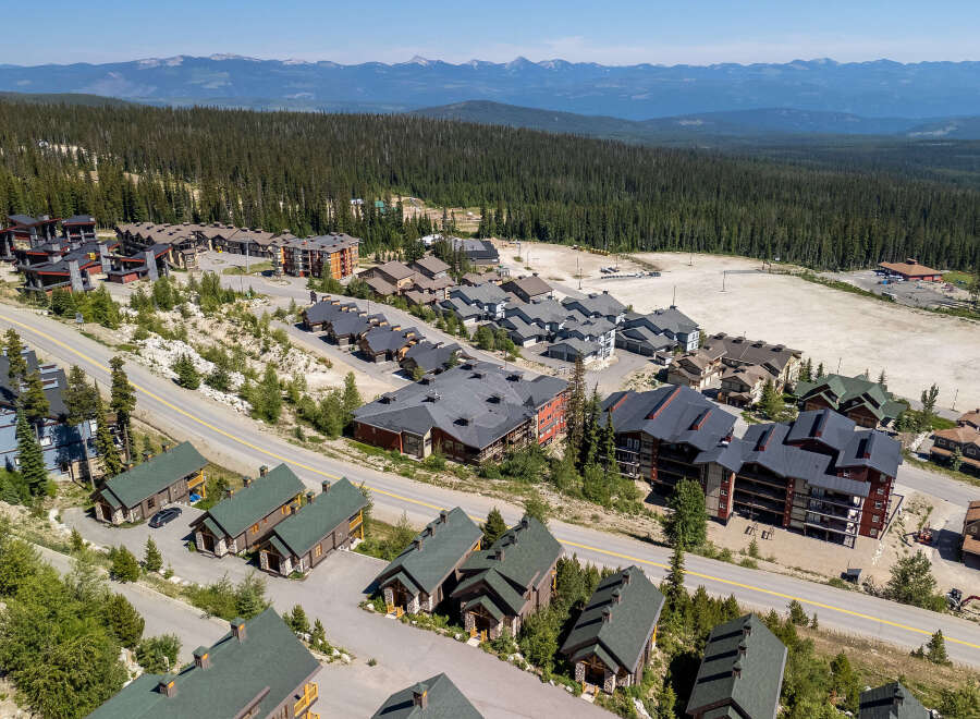 Discover this stunning mountain village featuring a collection of modern chalets and multi-story residences nestled amidst a dense evergreen forest.