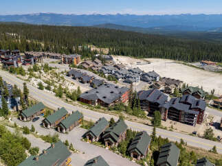 Discover this stunning mountain village featuring a collection of modern chalets and multi-story residences nestled amidst a dense evergreen forest.