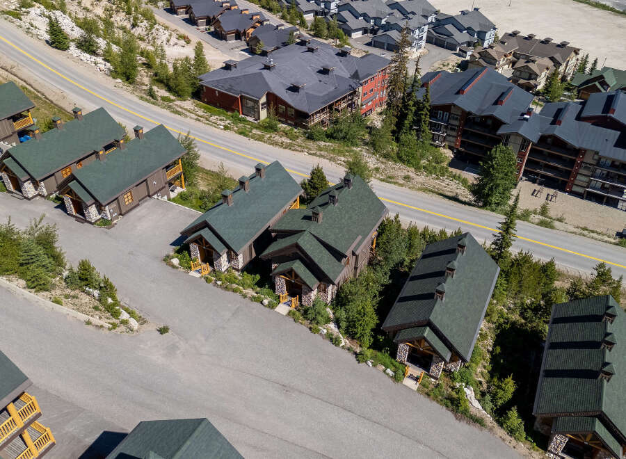 Discover this stunning mountain property featuring charming wooden chalets with stone accents and dark green roofs, nestled amidst lush greenery and winding roads.