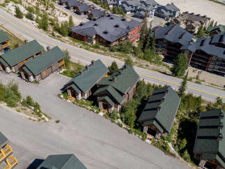 Discover this stunning mountain property featuring charming wooden chalets with stone accents and dark green roofs, nestled amidst lush greenery and winding roads.
