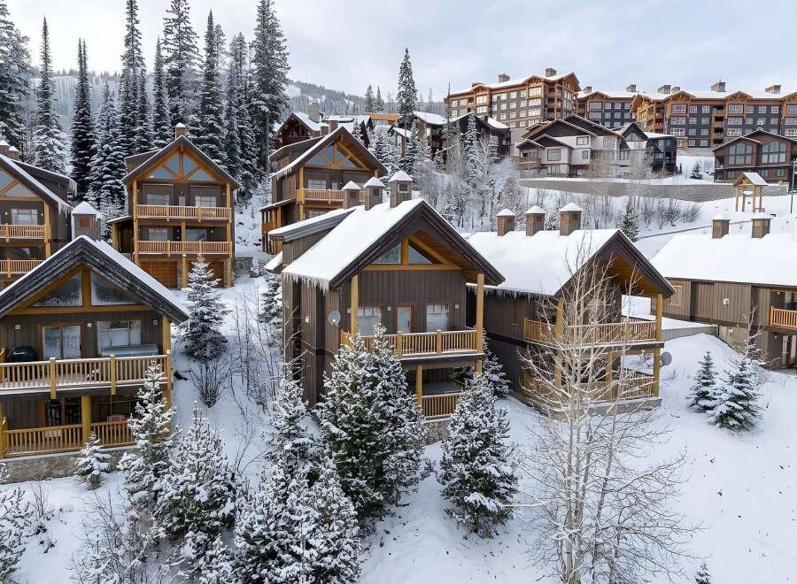 Experience luxury mountain living in this stunning ski resort property, featuring charming wooden chalets nestled amidst snow-covered pine trees.
