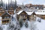 Experience luxury mountain living in this stunning ski resort property, featuring charming wooden chalets nestled amidst snow-covered pine trees.