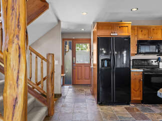 Experience rustic charm in this inviting entryway and kitchen area, featuring a grand log staircase and warm wooden cabinetry.