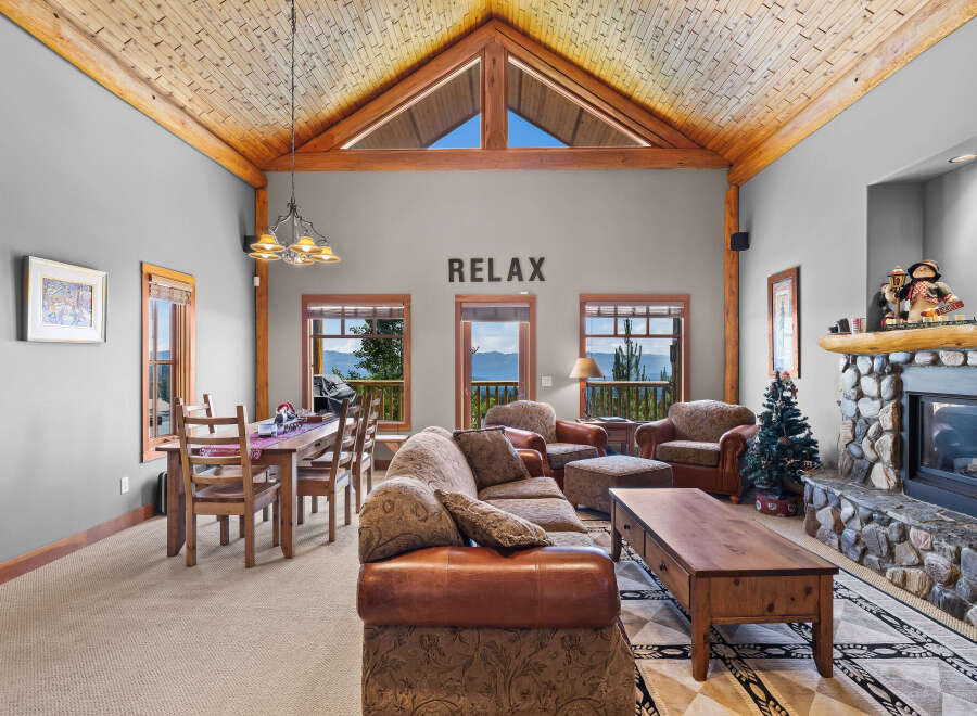 Experience breathtaking mountain views from this stunning living room, featuring a grand stone fireplace and a vaulted, wood-beamed ceiling.