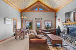 Experience breathtaking mountain views from this stunning living room, featuring a grand stone fireplace and a vaulted, wood-beamed ceiling.