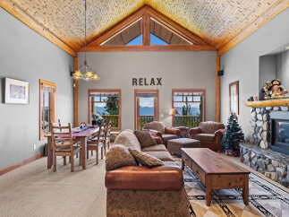 Experience breathtaking mountain views from this stunning living room, featuring a grand stone fireplace and a vaulted, wood-beamed ceiling.