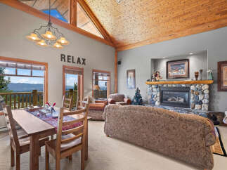 Experience breathtaking mountain views from this stunning living and dining area, featuring a cozy stone fireplace and a rustic wooden ceiling.