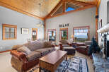 Experience breathtaking mountain views from this stunning living room, featuring a vaulted wood-paneled ceiling and a cozy stone fireplace.