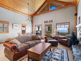 Experience breathtaking mountain views from this stunning living room, featuring a vaulted wood-paneled ceiling and a cozy stone fireplace.
