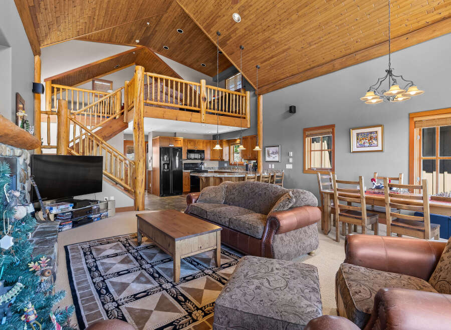 Experience rustic charm in this spacious living area featuring a soaring wood-paneled vaulted ceiling and a grand stone fireplace.
