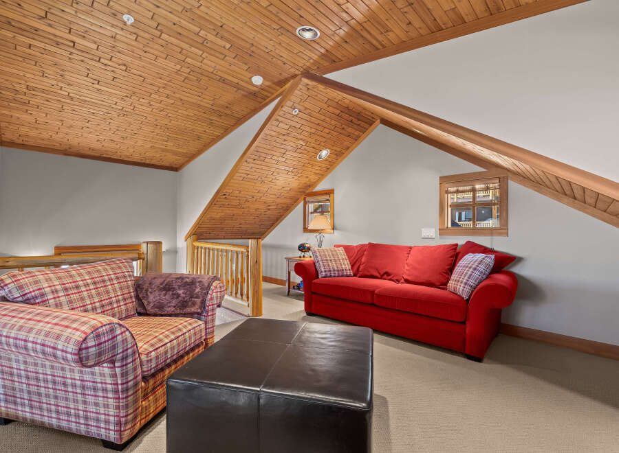 Cozy up in this charming attic living space, featuring a vibrant red sofa and a comfortable plaid armchair.