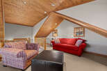 Cozy up in this charming attic living space, featuring a vibrant red sofa and a comfortable plaid armchair.