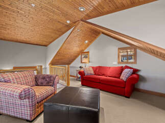 Cozy up in this charming attic living space, featuring a vibrant red sofa and a comfortable plaid armchair.
