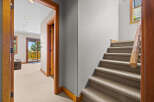 Step into this inviting space featuring a carpeted staircase with a rustic wooden handrail, leading to a bright hallway with a leather ottoman and a sliding glass door to a balcony.