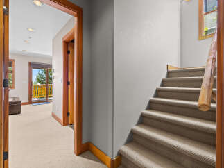 Step into this inviting space featuring a carpeted staircase with a rustic wooden handrail, leading to a bright hallway with a leather ottoman and a sliding glass door to a balcony.