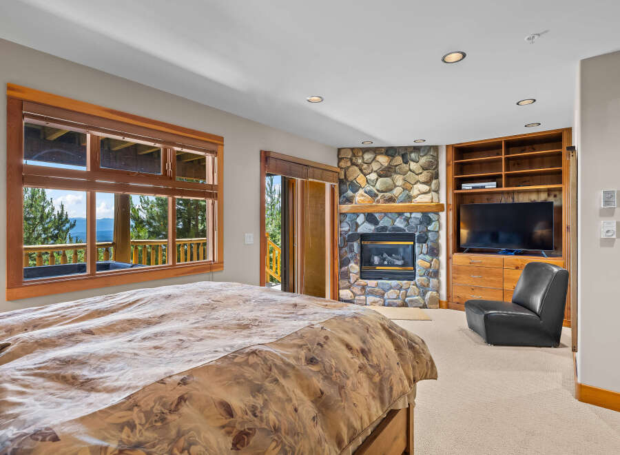 Experience ultimate comfort in this luxurious bedroom, featuring a stunning stone fireplace and a large window with breathtaking mountain views.
