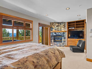Experience ultimate comfort in this luxurious bedroom, featuring a stunning stone fireplace and a large window with breathtaking mountain views.