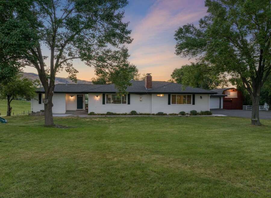 This charming white ranch-style home offers a picturesque setting with mature trees and a spacious lawn.