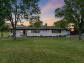This charming white ranch-style home offers a picturesque setting with mature trees and a spacious lawn.
