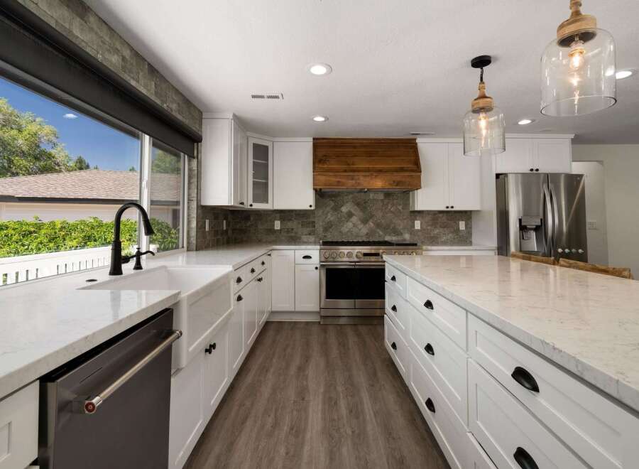 Experience modern luxury in this stunning kitchen, featuring sleek white cabinetry, a farmhouse sink, and a striking wood range hood.
